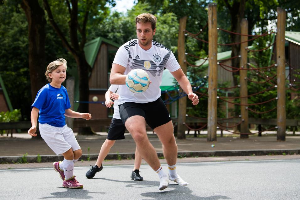 Ein Junge in blauer Sportkleidung dribbelt einen Ball, während ein älterer Spieler ihm entgegenkommt.